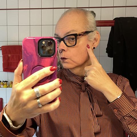 Mirror selfie of me making a duck face, pointing to the area of the sideburns, where my hair makes a soft wave down to vanish behind my ear.