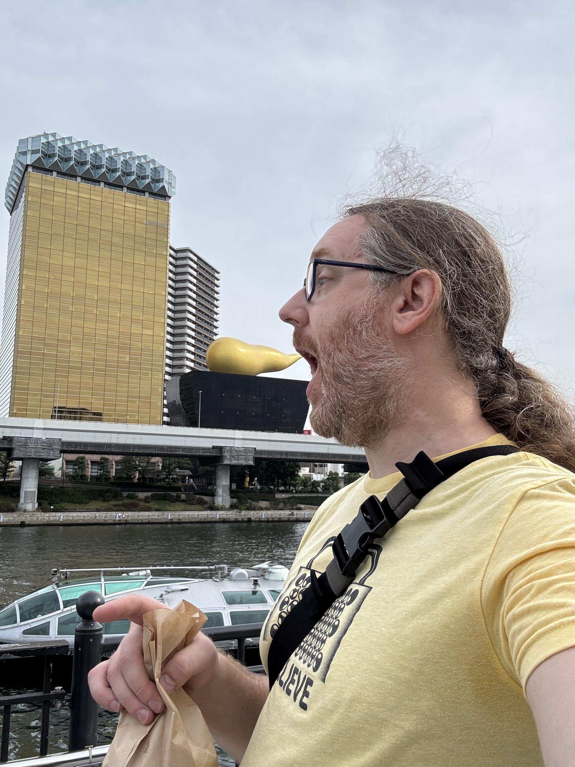 Selfie while pretending to eat a gold tiud shaped ornament on a building across the river