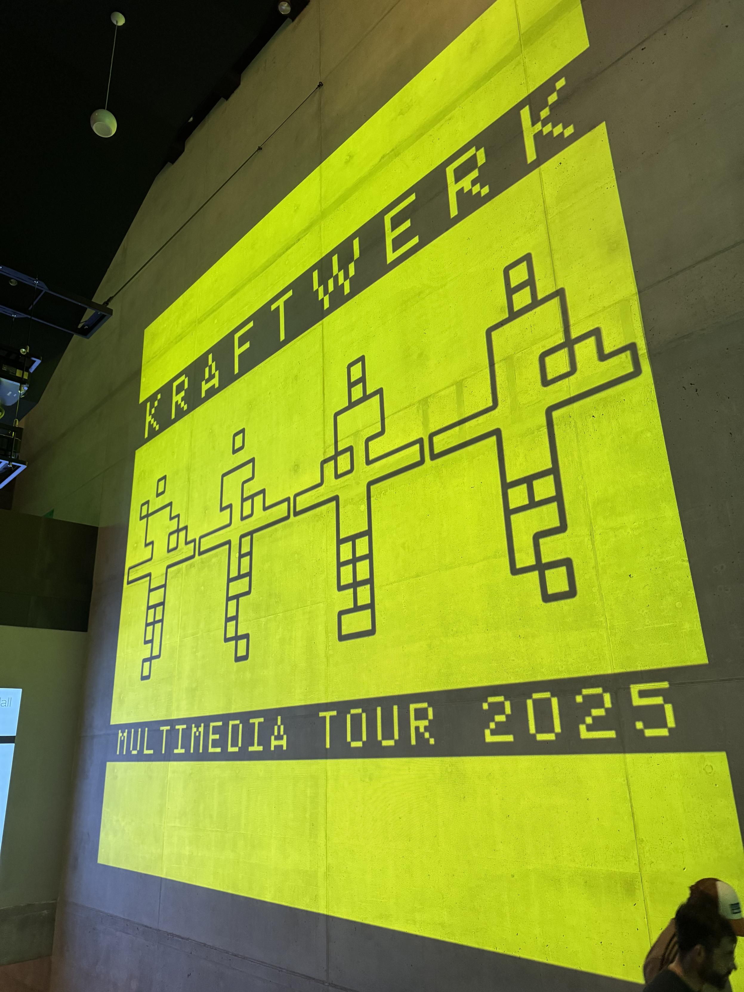 Yellow projection on concrete indoor wall announcing the Kraftwerk Multimedia Tour 2025
