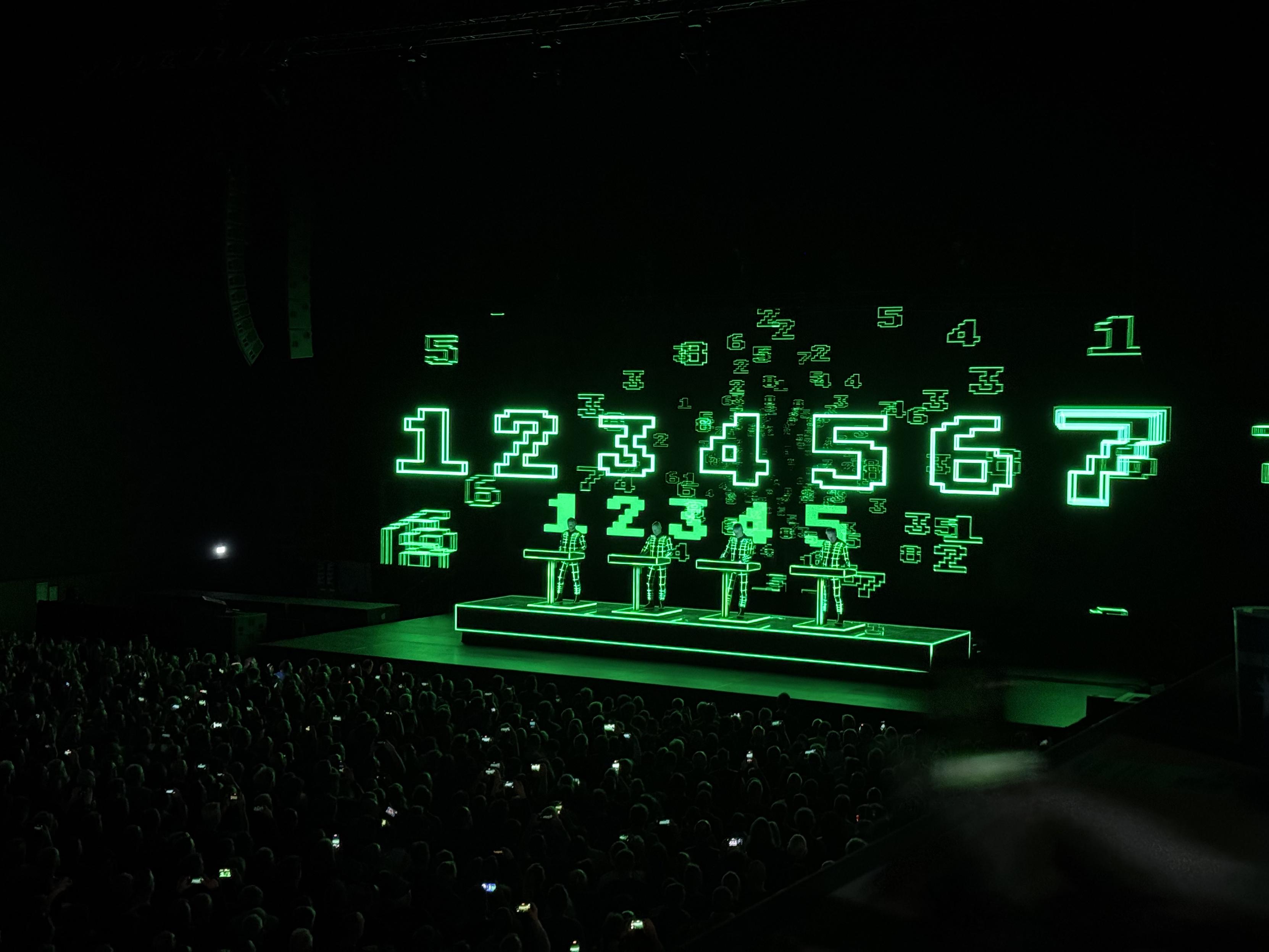 Green music stage projections showing the numbers 1-8 on black background with four musicians and their keyboards.